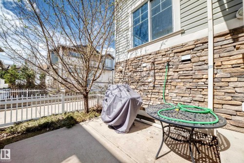 Concrete patio featuring a stone veneer exterior, a white picket fence, and a young deciduous tree - 45 4850 Terwillegar Common, Edmonton, AB - Outdoor