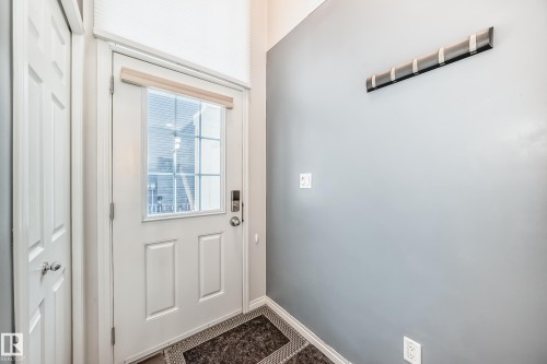 Entryway featuring a white paneled door with glass inserts, a digital lock, and a light-filtering cellular shade - 45 4850 Terwillegar Common, Edmonton, AB - Indoor Photo Showing Other Room