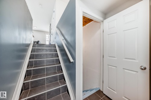 Staircase featuring dark tile treads with light grout, a white handrail, and a half wall in a neutral tone - 45 4850 Terwillegar Common, Edmonton, AB - Indoor Photo Showing Other Room