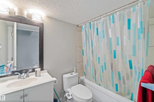 The bathroom features a vanity with a sink, a toilet, a bathtub, and a shower curtain - 1017 82 Street, Edmonton, AB - Indoor Photo Showing Bathroom