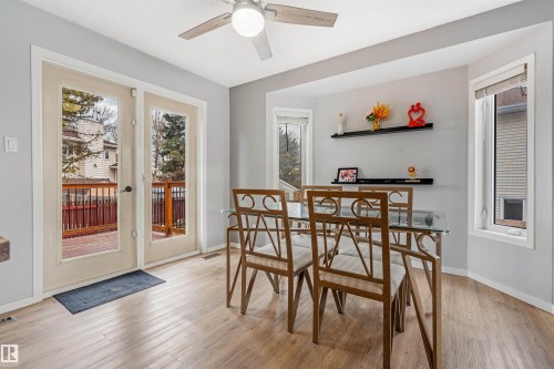 Light wood-finish flooring provides a neutral foundation for this room featuring a ceiling fan with integrated lighting, a bay window, and a pair of glass panel doors opening to a wood deck - 2437 89 Street, Edmonton, AB 