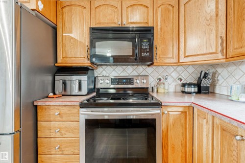 Kitchen featuring wood cabinetry, stainless steel appliances, a black over-the-range microwave, a tiled backsplash, and light-colored countertops - 2437 89 Street, Edmonton, AB 