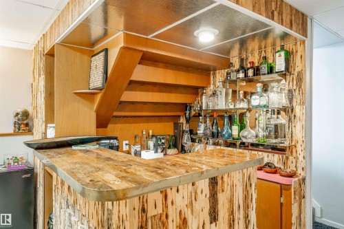 Custom bar area featuring a wood-finish countertop with metal trim, vertically paneled wood-finish walls, built-in shelving, and recessed lighting - 2437 89 Street, Edmonton, AB 