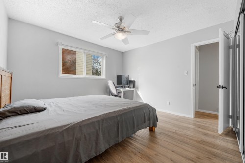 Bedroom featuring wood-finish flooring, a ceiling fan with integrated lighting, a window with horizontal blinds, and a paneled door - 2437 89 Street, Edmonton, AB 