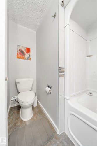 Bathroom featuring a white toilet, integrated shower/tub combination, and tiled flooring - 2437 89 Street, Edmonton, AB 