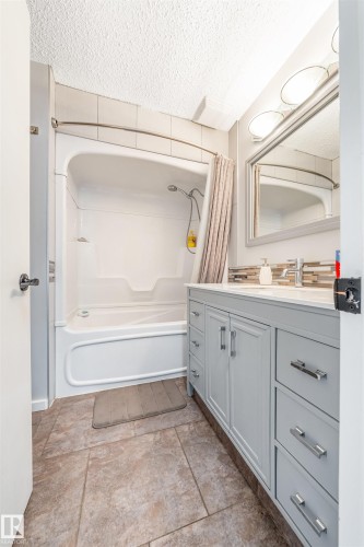 Bathroom featuring a white tub/shower combination, a light gray vanity with a white countertop, and tiled flooring - 2437 89 Street, Edmonton, AB 