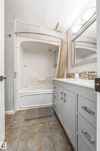 Bathroom featuring a light gray double vanity with white countertops, a tiled backsplash, and a shower-over-tub combination with white tile surround - 2437 89 Street, Edmonton, AB 