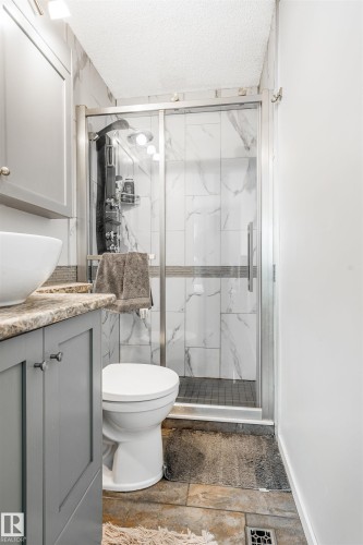 Bathroom featuring a glass-enclosed shower with white tiled walls and dark shower pan, a toilet, and gray cabinetry with a contrasting countertop and vessel sink - 2437 89 Street, Edmonton, AB 