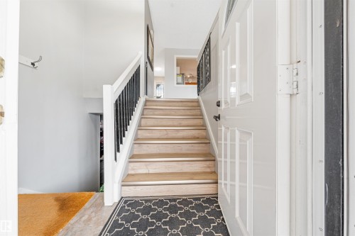 Inviting entryway featuring a paneled front door, wood-finish stairs with white risers, and a white handrail with black spindles - 2437 89 Street, Edmonton, AB 