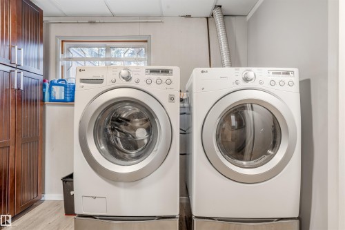 Dedicated laundry area featuring a white front-loading washer and dryer set on pedestals, complemented by built-in wood-finish cabinetry - 2437 89 Street, Edmonton, AB 