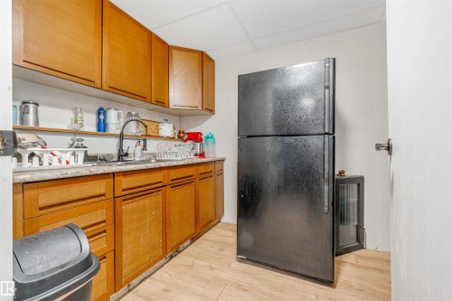 Kitchenette featuring wood-finish cabinetry, a black refrigerator, a wall-mounted faucet, and wood-finish flooring - 2437 89 Street, Edmonton, AB 