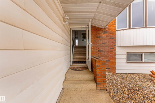 Exterior entryway featuring concrete steps, brick detailing, light-colored horizontal siding, and a gravel ground cover - 2437 89 Street, Edmonton, AB 