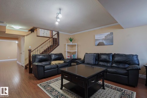 Open concept living area with wood-finish flooring, staircase with dark wood newel posts, and crown molding - 10731 150 Street Nw, Edmonton, AB - Indoor Photo Showing Living Room