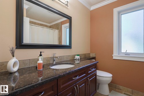 Bathroom featuring a dark wood-finish vanity with a built-in sink, dark stone countertop, and tile backsplash - 10731 150 Street Nw, Edmonton, AB - Indoor Photo Showing Bathroom