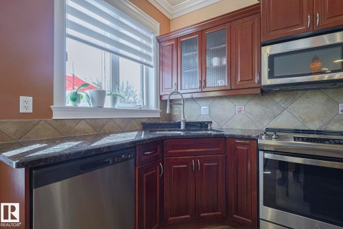 Kitchen featuring rich wood cabinetry, stainless steel appliances, dark speckled countertops, and a diagonal tile backsplash - 10731 150 Street Nw, Edmonton, AB - Indoor Photo Showing Kitchen With Double Sink