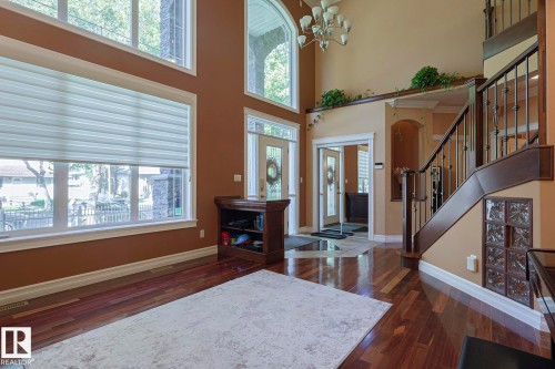 Spacious entry hall featuring wood-finish flooring, a grand staircase with decorative wrought iron spindles, high ceilings, large arched windows, and a multi-tiered chandelier - 10731 150 Street Nw, Edmonton, AB - Indoor Photo Showing Other Room