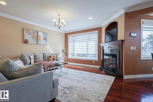 Living room featuring rich wood-finish flooring, a built-in fireplace with a decorative wood mantel and stone surround, and multiple windows with blinds - 10731 150 Street Nw, Edmonton, AB - Indoor Photo Showing Living Room With Fireplace