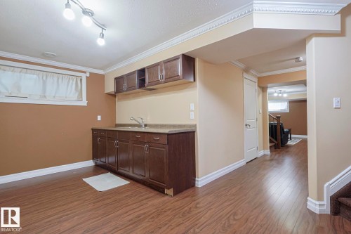 Lower-level kitchenette featuring wood-finish flooring, dark wood cabinetry, a sink with a chrome faucet, and a light-colored countertop - 10731 150 Street Nw, Edmonton, AB - Indoor Photo Showing Other Room