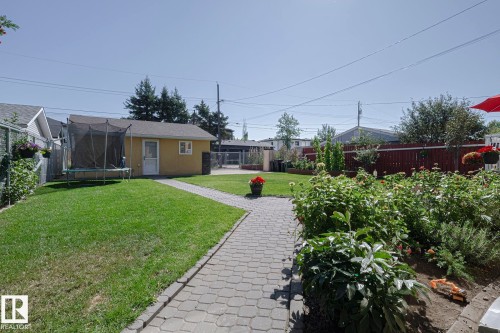 Expansive backyard featuring a paver stone pathway, a detached yellow outbuilding, mature perimeter fencing, and established garden beds with varied foliage - 10731 150 Street Nw, Edmonton, AB - Outdoor