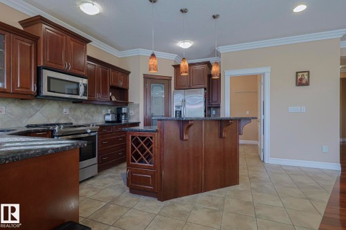Kitchen featuring extensive dark wood cabinetry, stainless steel appliances, speckled countertops, a tiled backsplash, and an island with an integrated wine rack - 10731 150 Street Nw, Edmonton, AB - Indoor Photo Showing Kitchen