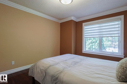 Spacious room featuring a large window with privacy blinds, dark wood-finish flooring, and crown molding - 10731 150 Street Nw, Edmonton, AB - Indoor Photo Showing Bedroom