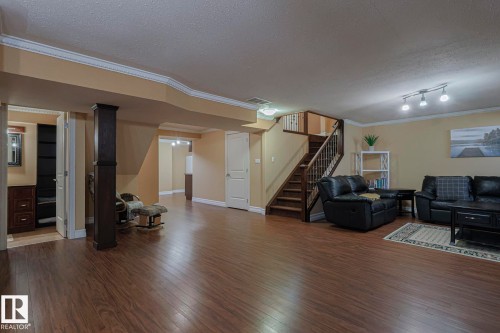 Spacious lower-level living area featuring wood-finish flooring, a dark wood staircase with matching railings, and recessed lighting - 10731 150 Street Nw, Edmonton, AB - Indoor