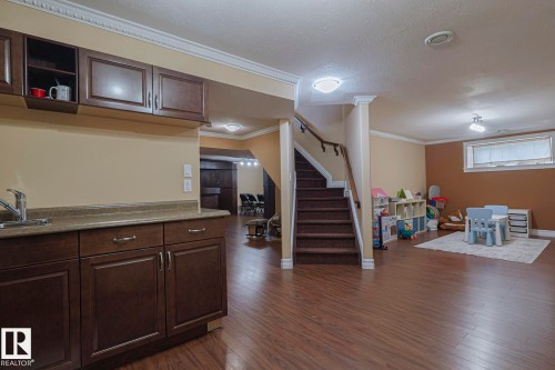 Lower level featuring wood-finish flooring throughout, a built-in wet bar with dark wood cabinetry and a countertop, a staircase with a wood handrail, and multiple recessed and surface-mounted light fixtures - 10731 150 Street Nw, Edmonton, AB - Indoor