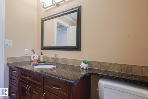 Bathroom featuring a dark wood-finish vanity with ample storage, a granite-style countertop, and an integrated white oval sink - 10731 150 Street Nw, Edmonton, AB - Indoor Photo Showing Bathroom
