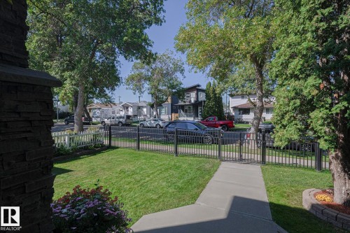 Manicured front yard with a concrete walkway, mature trees, and a black metal fence with a gate - 10731 150 Street Nw, Edmonton, AB - Outdoor