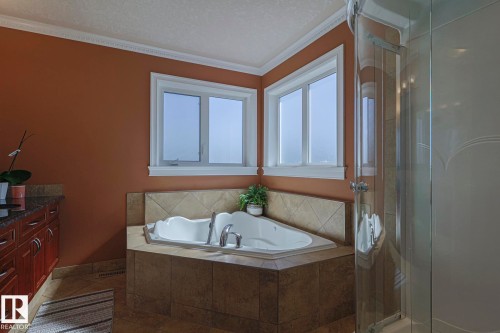 Corner jetted bathtub with a tiled surround, framed by two windows - 10731 150 Street Nw, Edmonton, AB - Indoor Photo Showing Bathroom
