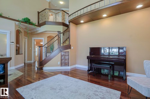 Open-concept living area featuring rich wood-finish flooring and a grand staircase with dark wood railings and balusters - 10731 150 Street Nw, Edmonton, AB - Indoor
