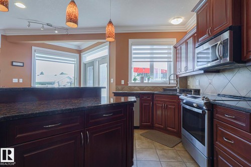 Kitchen featuring dark wood-finish cabinetry, stainless steel appliances, dark stone countertops, tile flooring, and a tile backsplash - 10731 150 Street Nw, Edmonton, AB - Indoor Photo Showing Kitchen