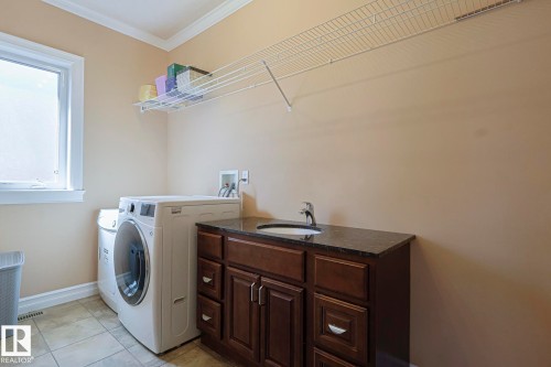 Dedicated laundry space featuring a utility sink, dark wood-finish cabinetry, and a stone-finish countertop - 10731 150 Street Nw, Edmonton, AB - Indoor Photo Showing Laundry Room