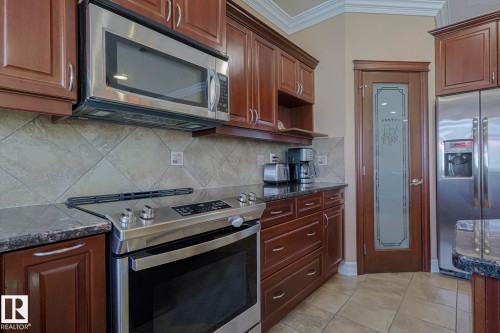 Kitchen featuring stainless steel appliances, dark wood cabinetry, and a pantry door with frosted glass detailing - 10731 150 Street Nw, Edmonton, AB - Indoor Photo Showing Kitchen