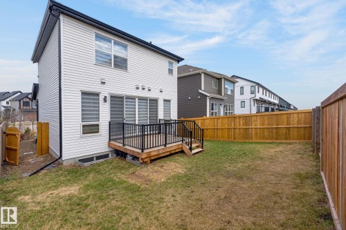 Rear exterior featuring white horizontal siding, a ground-level wood deck with black metal railings, and sliding glass doors - 1091 Secord Promenade, Edmonton, AB 