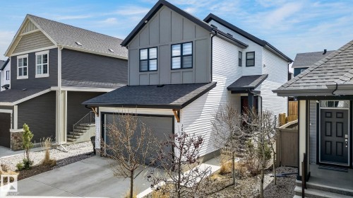 Contemporary two-story residence featuring a gray and white facade, prominent black-framed windows, and a black shingle roof - 1091 Secord Promenade, Edmonton, AB 