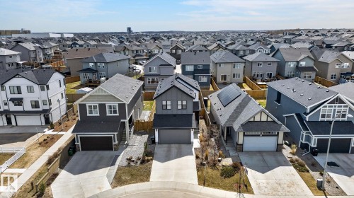Modern residential streetscape featuring a mix of two-story and single-story homes with attached garages, concrete driveways, and varying exterior finishes including siding and stone accents - 1091 Secord Promenade, Edmonton, AB 