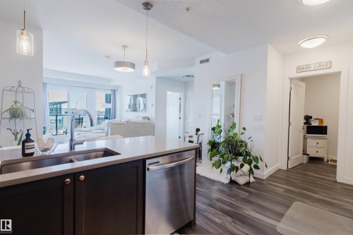 Open-concept living space featuring wood-finish flooring, a kitchen island with an undermount sink, stainless steel dishwasher, and contemporary pendant lighting - 316 1316 Windermere Way, Edmonton, AB - Indoor Photo Showing Kitchen With Double Sink