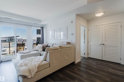 Living area featuring wood-finish flooring, a contemporary ceiling light fixture, and white louvered double doors - 316 1316 Windermere Way, Edmonton, AB - Indoor