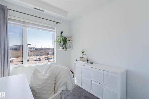 Bright room featuring a large window, white walls, gray carpet, and a built-in storage unit with pull-out bins - 316 1316 Windermere Way, Edmonton, AB - Indoor