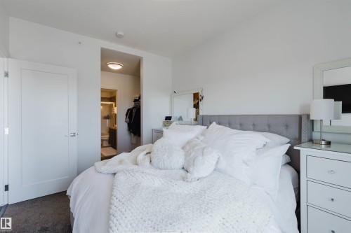 Carpeted bedroom featuring a tufted fabric headboard, white interior doors, and a recessed ceiling light - 316 1316 Windermere Way, Edmonton, AB - Indoor Photo Showing Bedroom