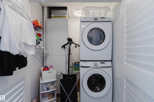 Dedicated laundry area featuring a white stacked washer and dryer unit, white louvered bifold doors, and overhead lighting - 316 1316 Windermere Way, Edmonton, AB - Indoor Photo Showing Laundry Room