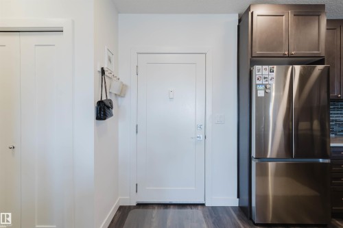 Entryway featuring wood-finish flooring, a white paneled door with brushed nickel hardware, and a built-in closet with bifold doors - 316 1316 Windermere Way, Edmonton, AB - Indoor Photo Showing Other Room