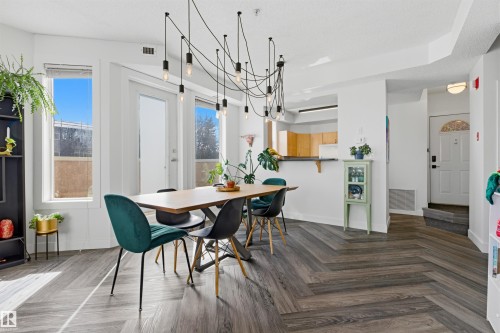 Dining area featuring herringbone wood-finish flooring, ample natural light from multiple windows and a glass-paneled door, and a multi-bulb pendant light fixture - 101 8108 109 Street, Edmonton, AB - Indoor Photo Showing Dining Room