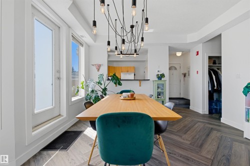 Dining area featuring wood-finish flooring in a herringbone pattern, a contemporary multi-bulb chandelier, and a built-in breakfast bar with a black countertop - 101 8108 109 Street, Edmonton, AB - Indoor Photo Showing Other Room
