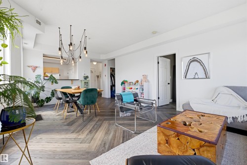 Open-concept living space with herringbone wood-finish flooring, a modern multi-bulb chandelier, a built-in breakfast bar, and white interior doors with black hardware - 101 8108 109 Street, Edmonton, AB - Indoor Photo Showing Living Room