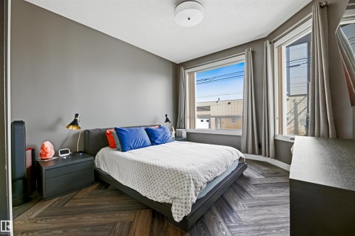 Bedroom featuring dark wood-finish flooring in a herringbone pattern, neutral wall paint, and multiple windows - 101 8108 109 Street, Edmonton, AB - Indoor Photo Showing Bedroom