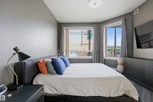 Bedroom featuring two large windows, dark wood-finish flooring, a contemporary ceiling light fixture, and a wall-mounted flat-screen television - 101 8108 109 Street, Edmonton, AB - Indoor Photo Showing Bedroom