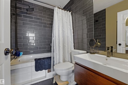 Bathroom featuring dark subway tile shower surround, a tub with a dark-finish rainfall showerhead, a floating vanity with a vessel sink, and a framed mirror - 101 8108 109 Street, Edmonton, AB - Indoor Photo Showing Bathroom