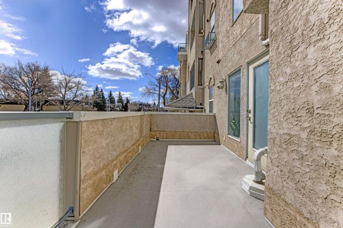 Expansive private patio featuring a concrete surface, stucco exterior walls, and a partial glass railing - 101 8108 109 Street, Edmonton, AB - Outdoor